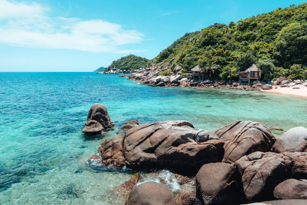 Clear water, rocky beach, lush greenery.