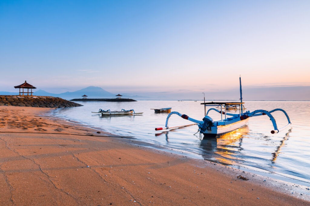 Calm beach with fishing boats at sunrise.
