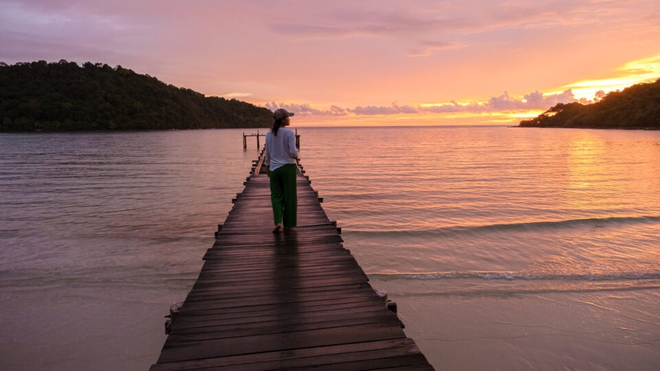 Person walking on wooden pier at sunset