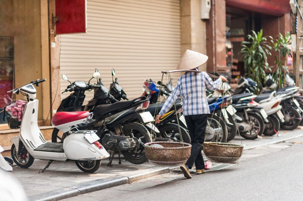 Woman carrying baskets near parked motorcycles.