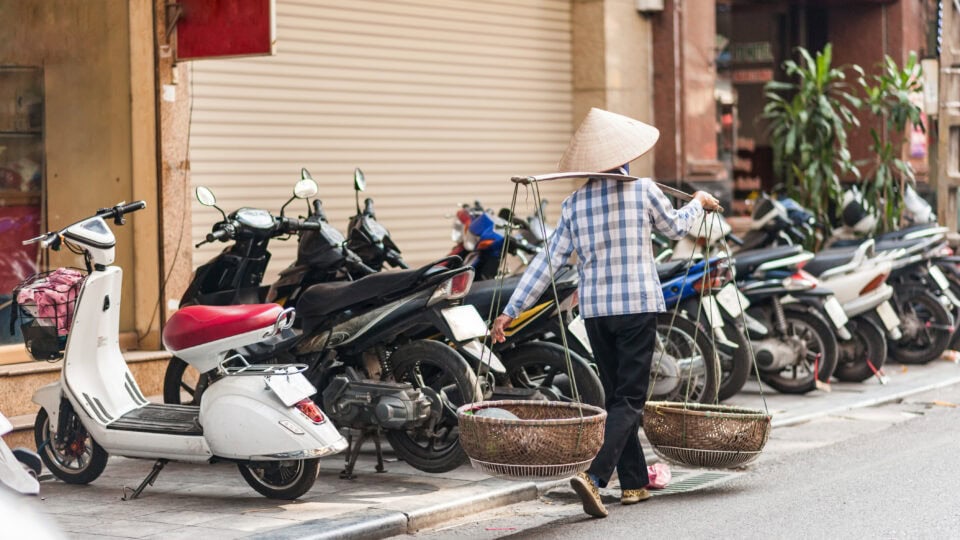 Woman carrying baskets near parked motorcycles.